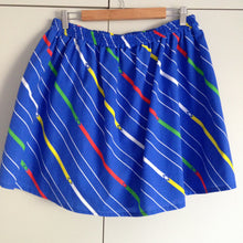 Load image into Gallery viewer, Back view of blue skirt. The fabric has diagonal stripes in white, yellow, green and red.
