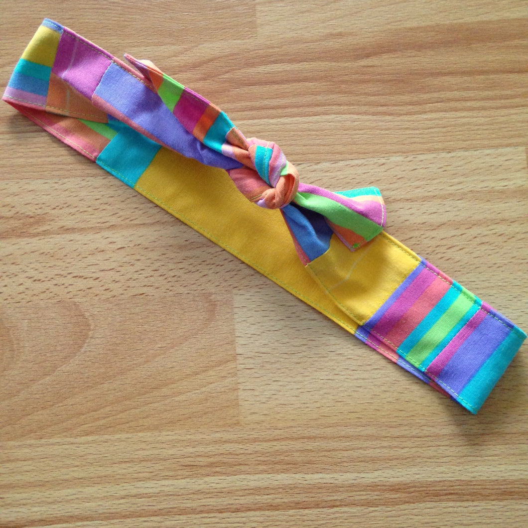 Candy coloured stripe headband tied in a bow. Centre (back) of the headband has a big yellow section.