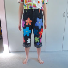 Load image into Gallery viewer, black denim 3/4 length jeans with multicoloured 60s style flowers. hem cuffs have embroider black flowers. worn with a white shirt with colourful swatch squares
