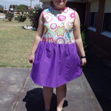 Load image into Gallery viewer, Front view of dress on model. The dress has a purple gathered skirt and sleeveless multicoloured bodice. The bodice has a geometric pattern that looks floral.

