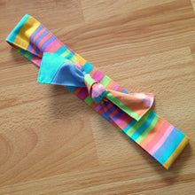 Load image into Gallery viewer, Candy coloured stripe headband tied in a bow. Part of the bow has a blue patch from the same fabric
