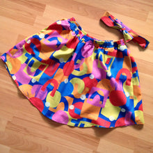 Load image into Gallery viewer, Flat lay of brightly coloured geometric patterned skirt with matching headband.
