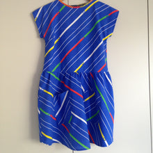 Load image into Gallery viewer, Front view of blue dress with pockets. The fabric has diagonal stripes in white, yellow, green and red.
