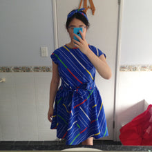 Load image into Gallery viewer, Try on of blue dress with belt and matching headband with pockets and stripes in white, green and red.
