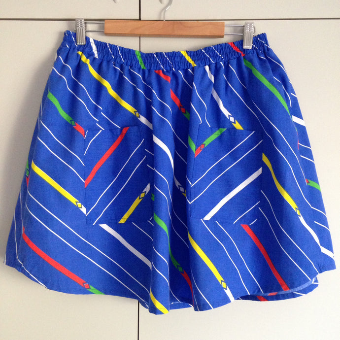 Front view of blue skirt with pockets. The fabric has diagonal stripes in white, yellow, green and red.