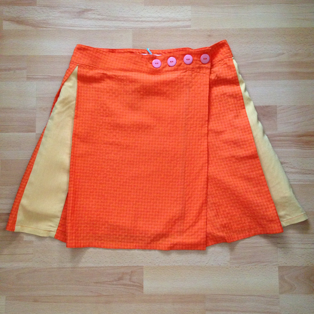 Front view of orange check wrap skirt with pink buttons and yellow contrast pleats.