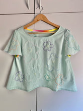 Load image into Gallery viewer, pale mint short sleeve top with 60s style stitched flowers in pastel colours and deep purple. Neck binding on the inside is a rainbow gradient.
