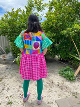 Load image into Gallery viewer, Dress with multicoloured geometric print bodice, frilly green and blue gingham sleeves and hot pink check skirt. Worn with green tights.
